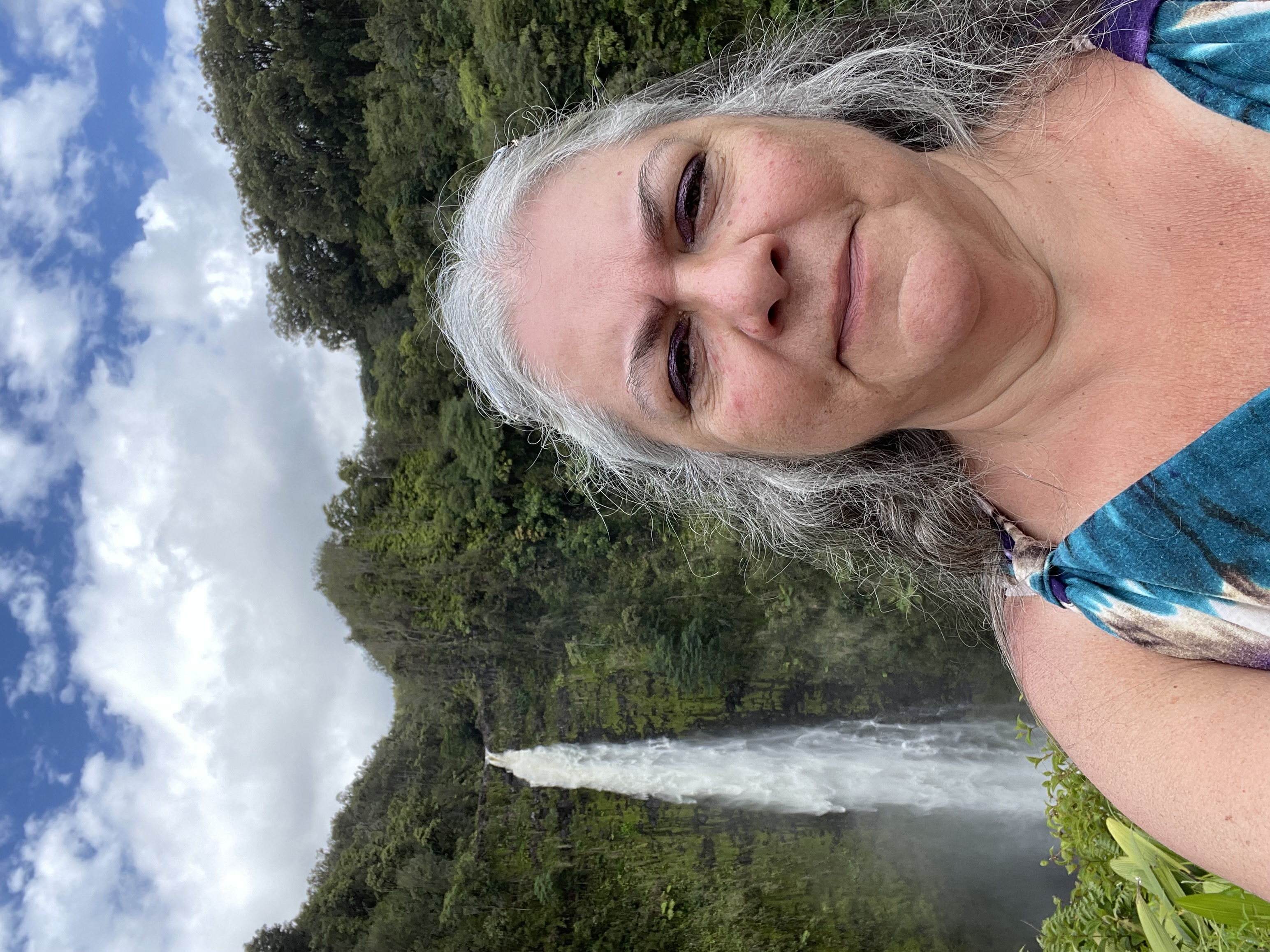 white female with long grey hair , waterfall behind her