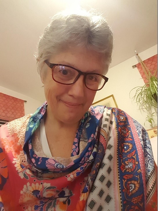 Female with short grey hair, dark glasses,  nice smile, colorful scarf