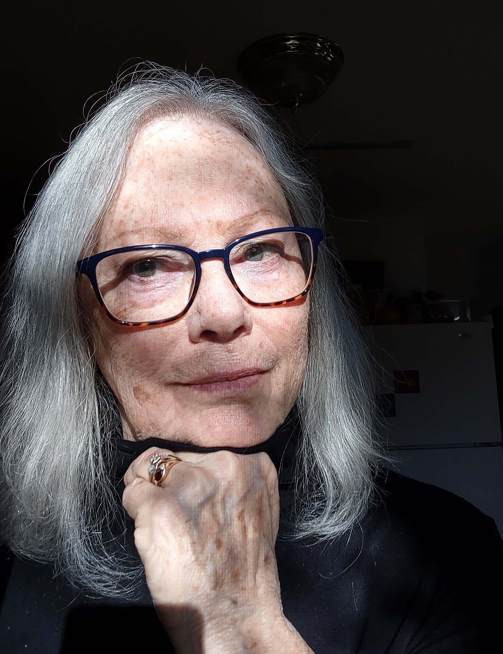 white woman with shoulder length grey hair, glasses, hand under chin