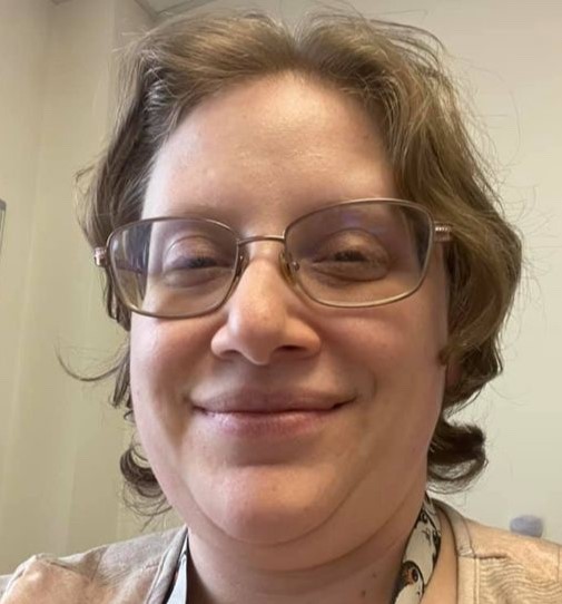 woman with glasses and short light colored hair. tan top.