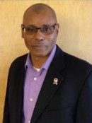 Black man with glasses, lavender shirt and dark suit coat