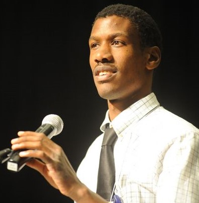 Man of color with microphone, white shirt, short cropped hair