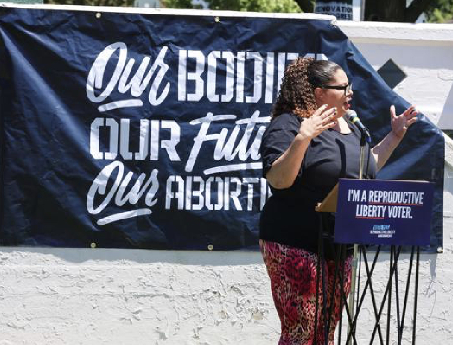 Woman of color standing at a podium speaking