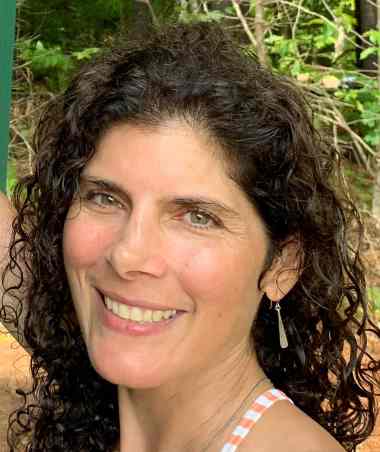 Female with long dark curly hair and a big smile