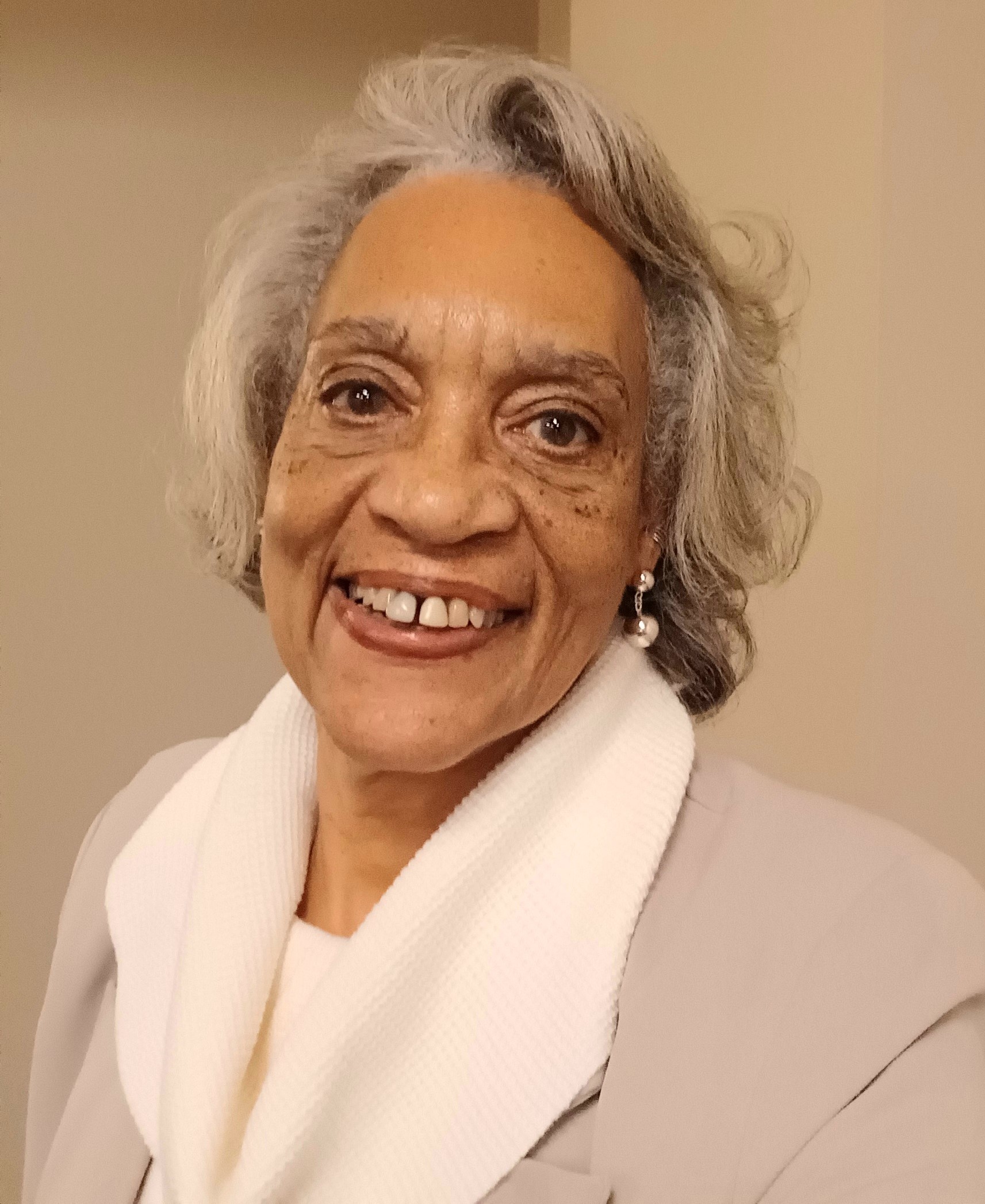 woman of color, short grey hair, white scarf and tan coat