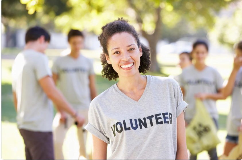 Light skinned Black Woman smiling with curly hair and shirt with Volunteer on it